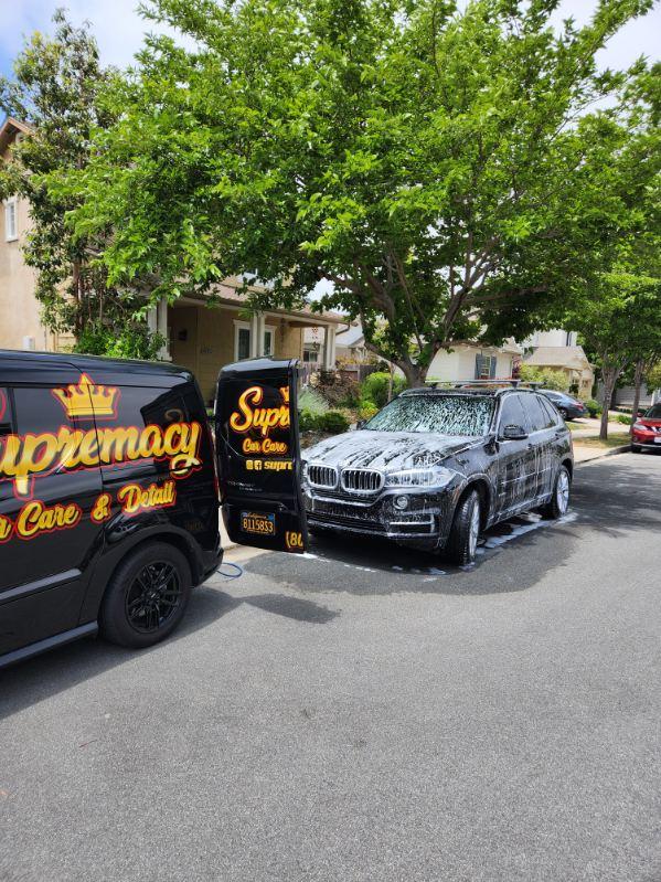 Supremacy van beside a black BMW SUV during a mobile detail